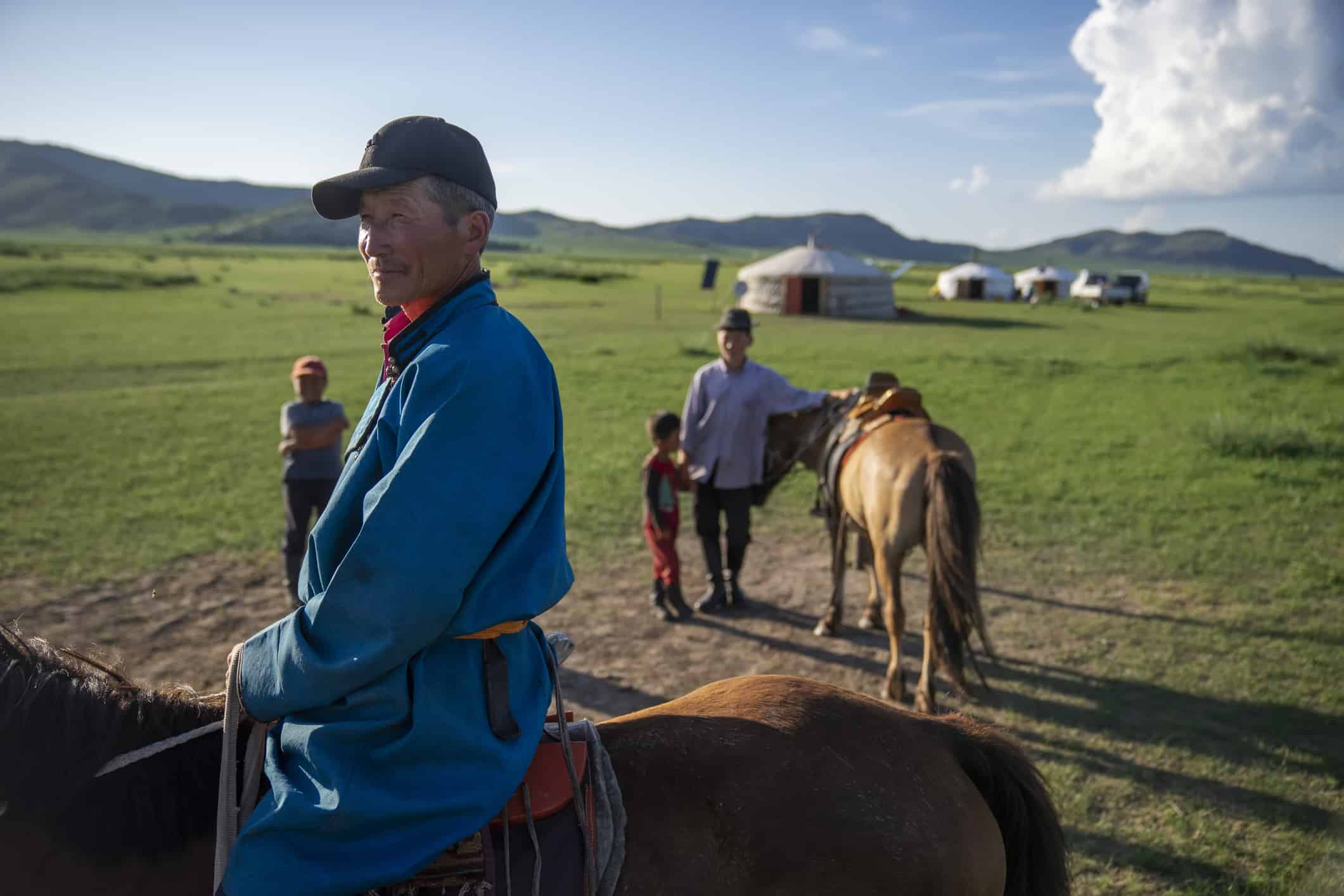 A nomadic family from the steppe in mongolia sitting on horse back in front of their traditional yurts
